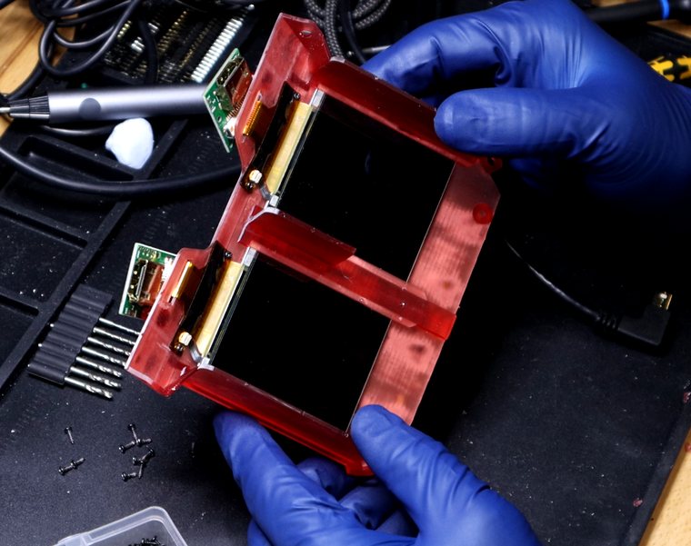 The stereoscopic display assembly held in gloved hands — two micro-displays in a red 3D-printed frame